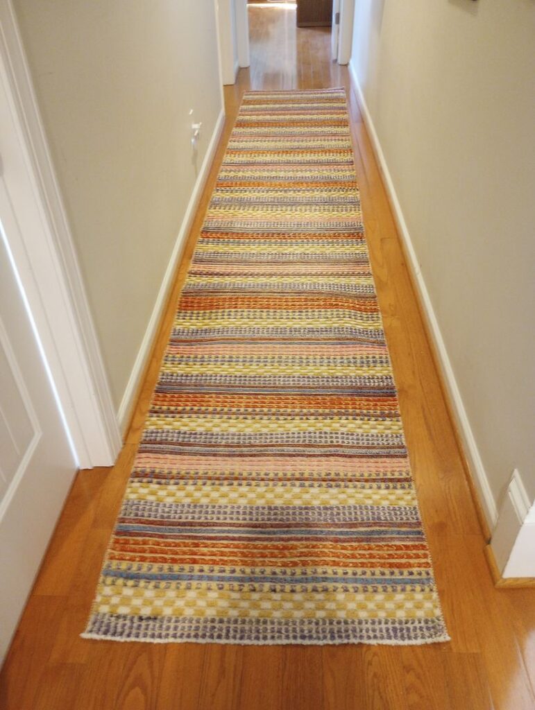 A colorful striped rug in a hallway with hardwood floors and light-colored walls